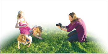 엄마가 풀밭에서 놀고 있는 세 딸 아이를 사진 찍고 있는 사진